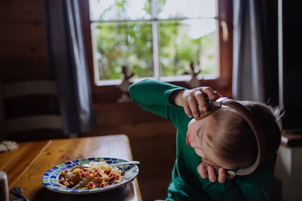 ダウン症の少年はヘッドフォンで昼食を持っていると自宅でカメラを見て. — ストック写真