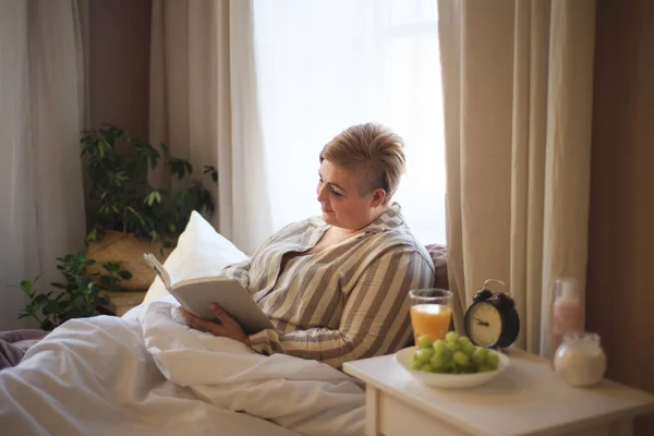 Щаслива надмірна вага жінка читає книгу в ліжку вдома . — стокове фото