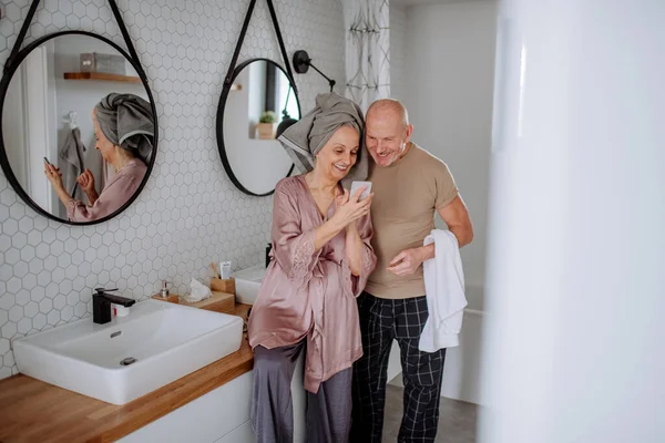 Idős pár szerelmes fürdőszobában, okostelefon használata, reggeli rutin koncepció. — Stock Fotó