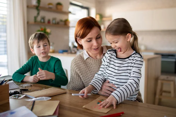 Мати маленьких дітей контролює їх, коли занурюється домашнє завдання вдома . — стокове фото