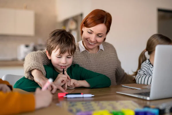Moeder van kleine kinderen die thuis op laptop werken bij afstandsonderwijs en kunstwerken. — Stockfoto