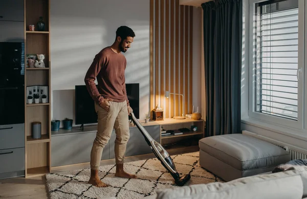 Fiatal férfi porszívó szőnyeg porszívóval a nappaliban — Stock Fotó