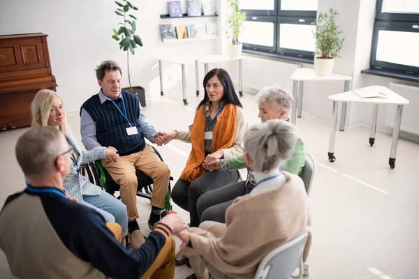 Группа пожилых людей, сидящих в кругу во время сеанса терапии, держащихся за руки и молящихся вместе. — стоковое фото