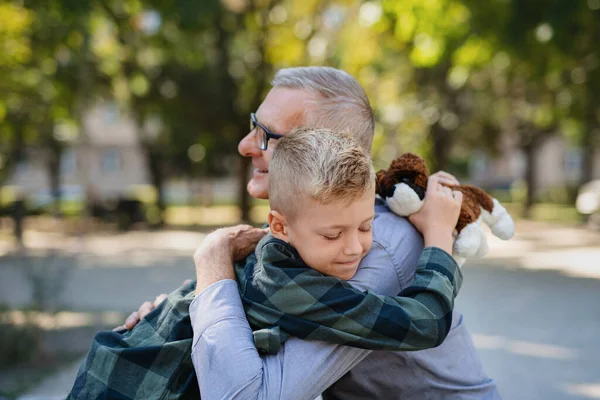 Šťastný malý chlapec objímající svého dědečka venku v parku. — Stock fotografie