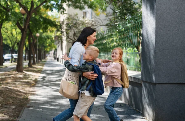 Niños felices corriendo hacia su abuela esperándolos después de la escuela al aire libre en la calle. — Foto de Stock