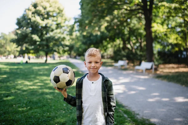 Счастливый маленький мальчик держит мяч и смотрит в камеру в парке. — стоковое фото