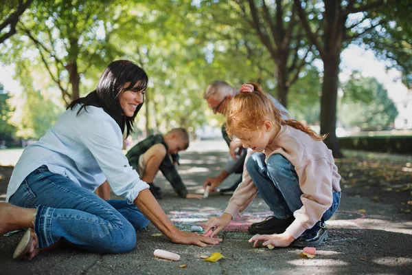 Senior couple with grandchildren drawing with chalks on pavement outdoors in park. — Stock Photo, Image