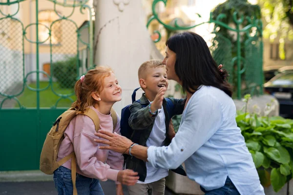 幸せな子供たち抱擁彼らの祖母待っています彼女の後に学校屋外で通り. — ストック写真