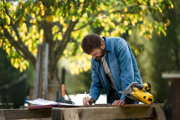 Homme à tout faire mesurant une planche, dehors dans le jardin. — Photo