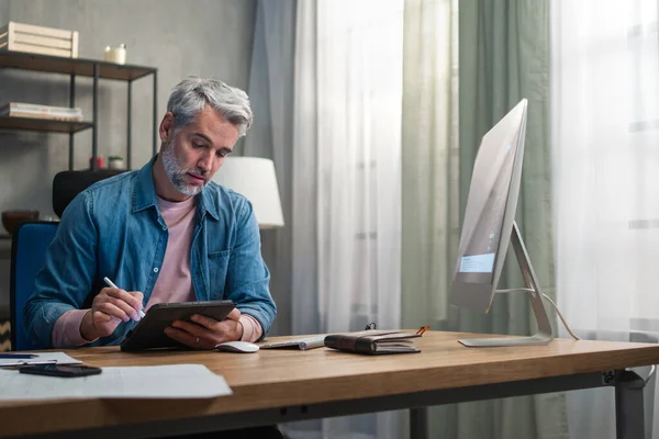 Volwassen man architect werkt op de computer aan het bureau binnen in het kantoor. — Stockfoto