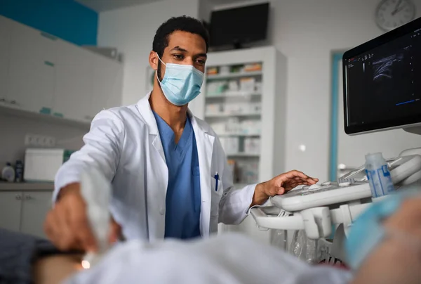 Tânărul medic examinează pacientul folosind un echipament cu ultrasunete în clinică, conceptul de coronavirus. — Fotografie, imagine de stoc