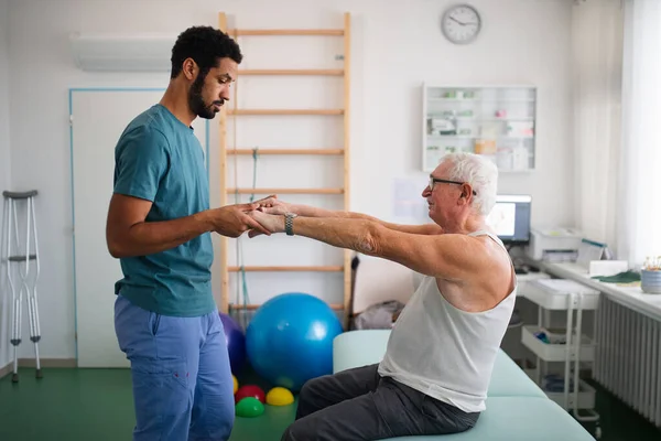 Jeune physiothérapeute faisant de l'exercice avec un patient âgé dans une salle de physiothérapie — Photo