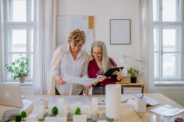 Femmes mûres éco architectes avec modèle de bâtiments modernes et des plans de travail ensemble dans le bureau. — Photo