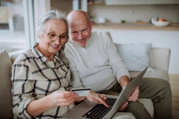 Pasangan senior duduk di sofa dan belanja online dengan laptop dan kartu kredit — Stok Foto