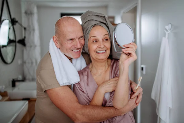 上了年纪的夫妻在浴室里谈恋爱，看着镜子和微笑，早上例行公事的概念. — 图库照片