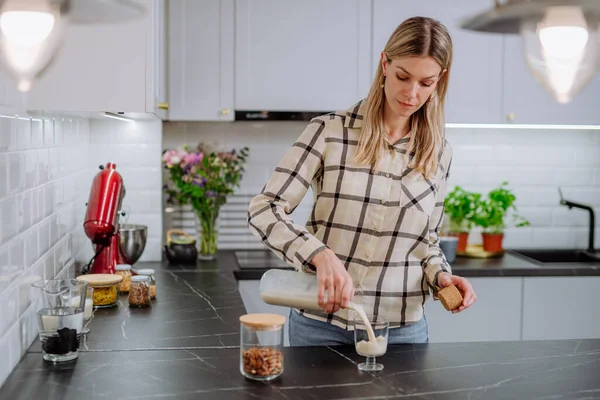 Mujer vertiendo leche de almendras en un vaso en la cocina. Concepto de producto vegano saludable. —  Fotos de Stock