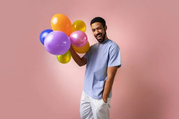 快乐的年轻儿科医生拿着粉色背景的气球 — 图库照片
