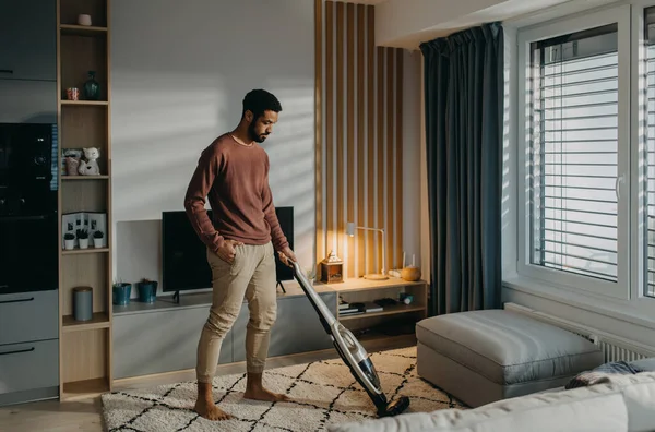 Jonge man stofzuigen tapijt met stofzuiger in de woonkamer — Stockfoto
