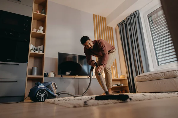 Jeune homme hoovering tapis avec aspirateur dans le salon — Photo