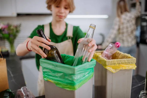 Adolescente chica lanzando botellas de vidrio en la papelera de reciclaje en la cocina. — Foto de Stock