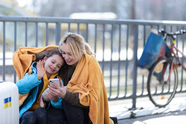 Ukrán bevándorlók anya lánya poggyász vár a vasútállomáson, ukrán háborús koncepció. — Stock Fotó