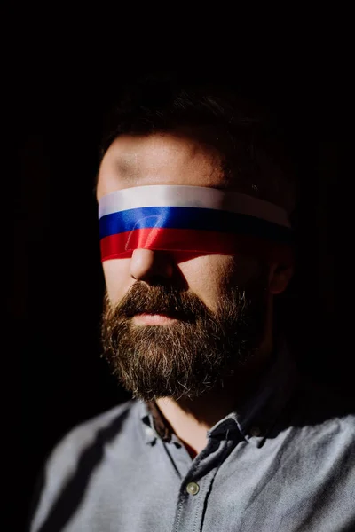 Hombre con bandera rusa venda en el fondo negro, propaganda rusa cerró los ojos de la gente concepto. — Foto de Stock