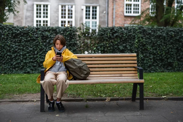 Школьница сидела на скамейке и пользовалась смартфоном на улице в городе. — стоковое фото