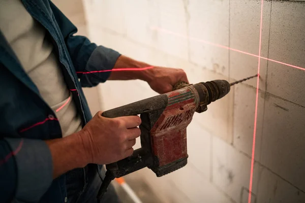 Nahaufnahme eines Heimwerkers, der mit Hilfe eines Lasernivellierers ein Loch mit Bohrer an der Wand macht — Stockfoto