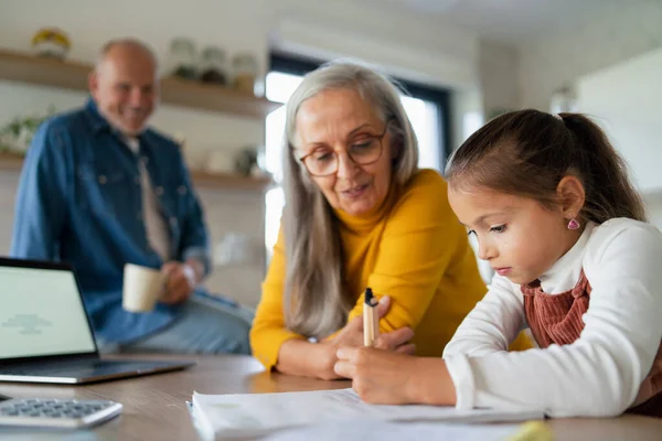 Klein meisje met senior grootouders doen wiskunde huiswerk thuis. — Stockfoto