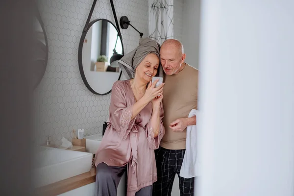 Senior par kär i badrummet, med hjälp av smartphone, morgon rutin koncept. — Stockfoto