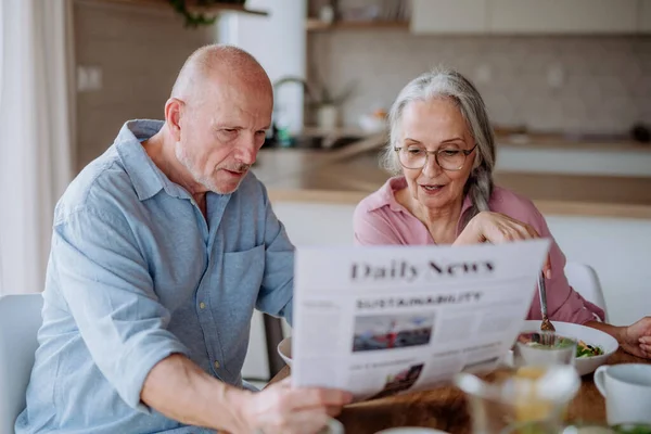 Happy senior couple having breakfast and reading newspaper together at home. — стоковое фото