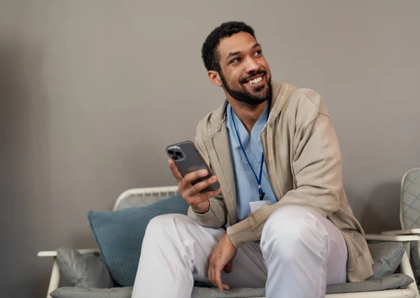 Ευτυχισμένος νεαρός άνδρας γιατρός ή φροντιστής με το smartphone χαλάρωση. — Φωτογραφία Αρχείου