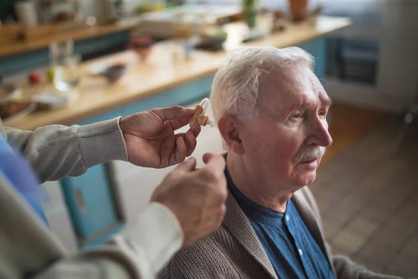 Caregiver helping senior man to insert hearing aid in his ear. — Stock Photo, Image