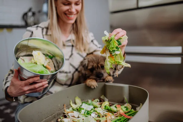 Kobieta rzuca sadzonki warzyw do wiadra kompostu w kuchni i karmi psa. — Zdjęcie stockowe