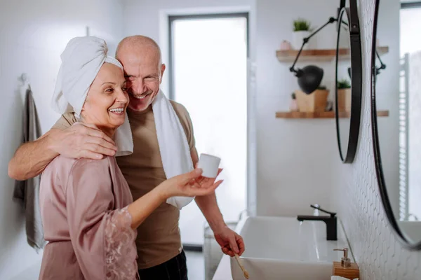 Casal de idosos apaixonados no banheiro, escovando os dentes e abraçando, conceito de rotina matinal. — Fotografia de Stock