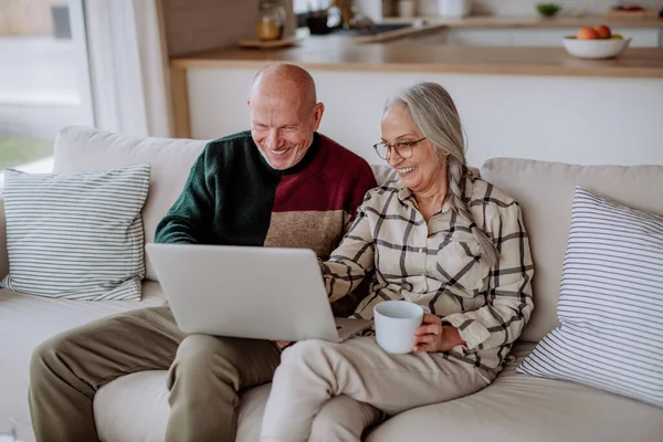 Couple âgé assis sur le canapé et faire du shopping en ligne avec ordinateur portable. — Photo