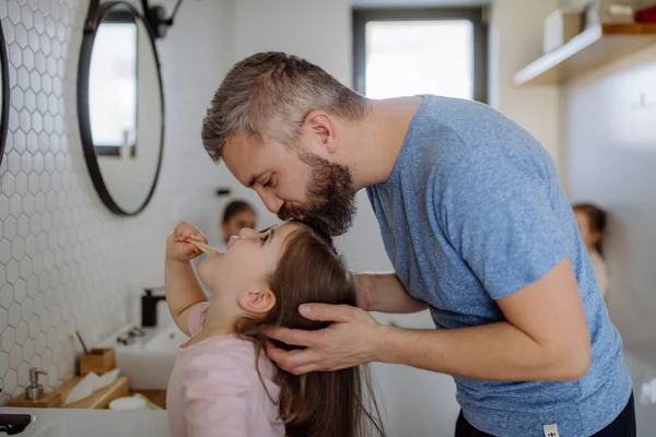 Padre baciare la figlia mentre lei si lava i denti in bagno, mattina concetto di routine. — Foto Stock