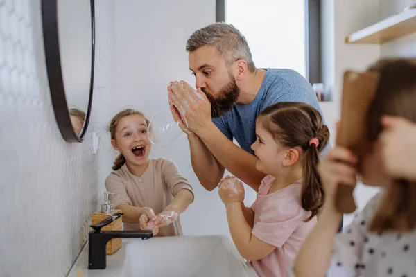 Father having fun blowing bubbles from soap in bathroom with his little daughters. — Foto de Stock