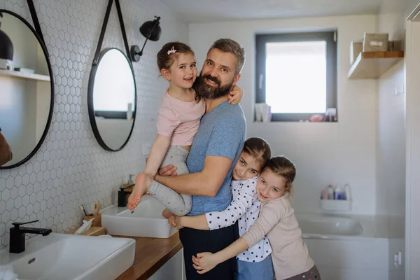 Отец сближается со своими тремя маленькими дочерьми в ванной и смотрит в камеру. — стоковое фото
