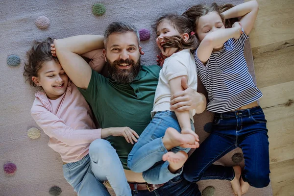 Top view of cheerful father with three little daughters lying on floor together at home.