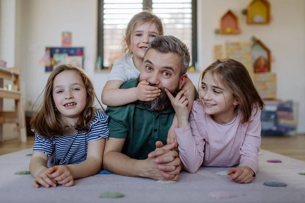 Mutlu bir baba ve üç küçük kızı evde birlikte yerde yatıyor.. — Stok fotoğraf
