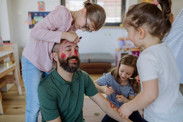 Three little girls putting on make up on their father, fathers day with daughters at home. — Stok fotoğraf