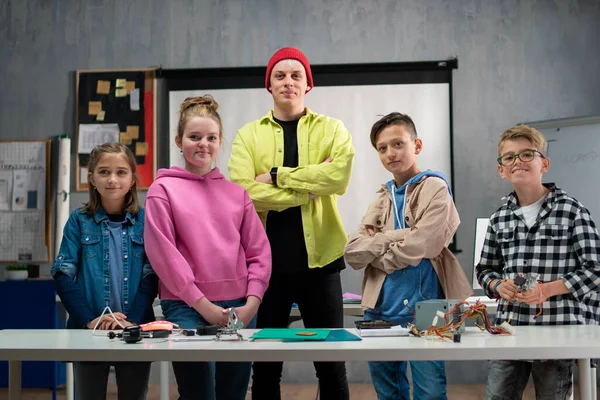 Group of happy kids with their science teacher with electric toys and robots at robotics classroom — стоковое фото