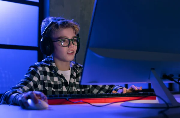 Ung spelare pojke med hörlurar spelar dataspel. — Stockfoto