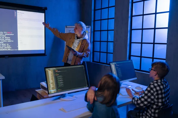 Teacher giving computer science lecture to young students in dark room. Room. Explaining Information Technology. — ストック写真