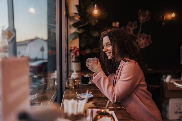 Young woman drinking tea and looking out of the cafe window while enjoying her leisure time alone — Foto Stock
