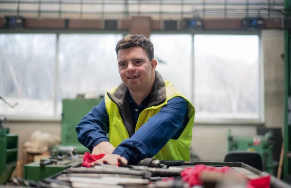 Joven con síndrome de Down trabajando en fábrica industrial, concepto de integración social. — Foto de Stock