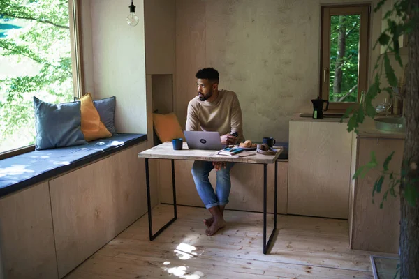 Jovem feliz com laptop sentado, descansando dentro de casa em uma casa de árvore, fim de semana longe e escritório remoto — Fotografia de Stock