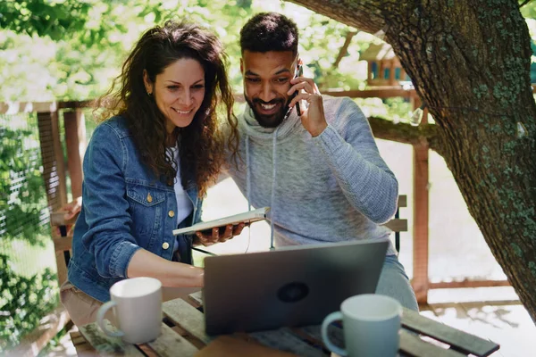 Glückliches Paar mit Laptop im Freien in einem Baumhaus, Wochenendausflug und abgelegenem Bürokonzept. — Stockfoto
