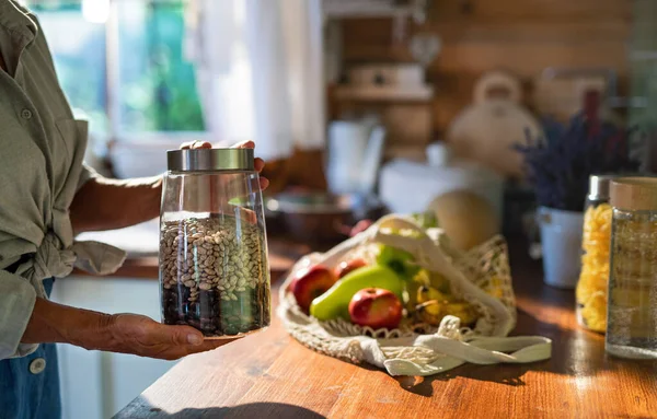 Primer plano de la mujer mayor desempacando alimentos locales en envases de residuos cero de la bolsa en la cocina en casa. —  Fotos de Stock